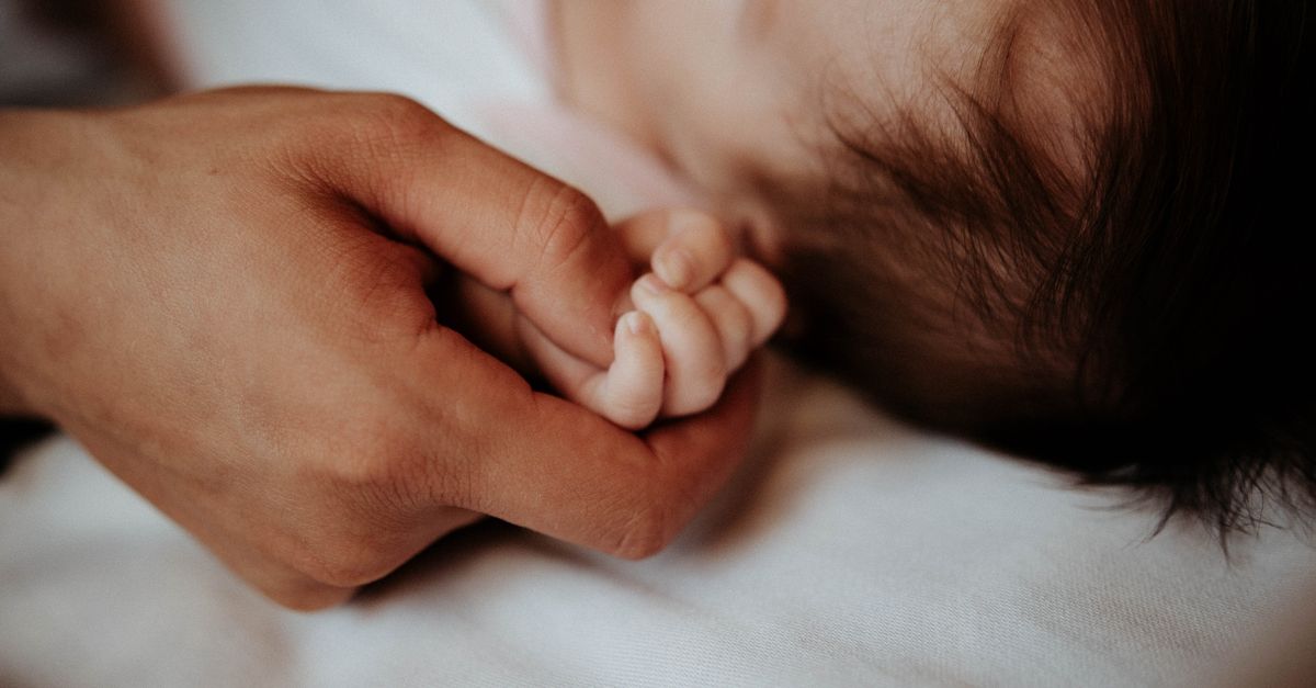 Close-up of a baby's hand gently held by a parent, symbolizing love and care.