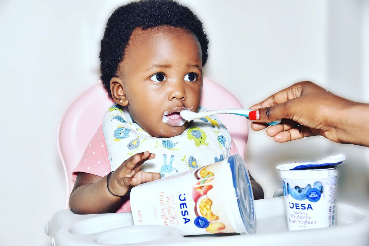 Baby in a high chair being spoon-fed first solid foods