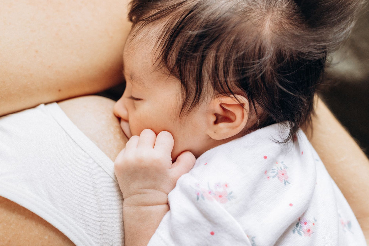 A newborn baby breastfeeds, resting a tiny hand against their cheek