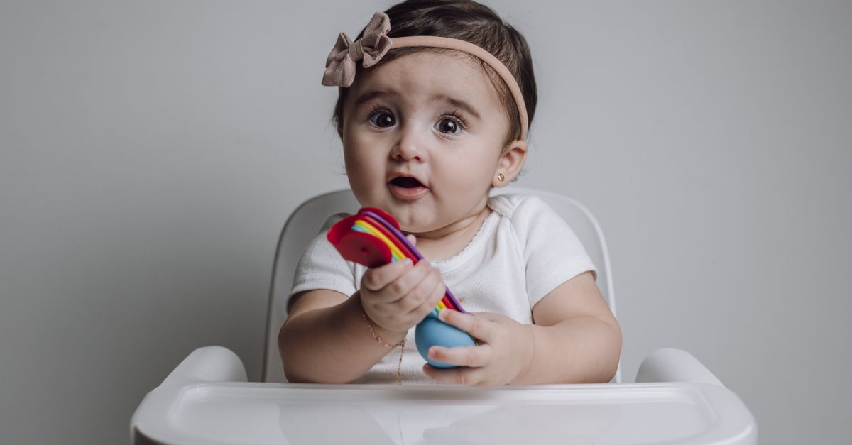 A baby sitting in a high chair holding colourful spoons.
