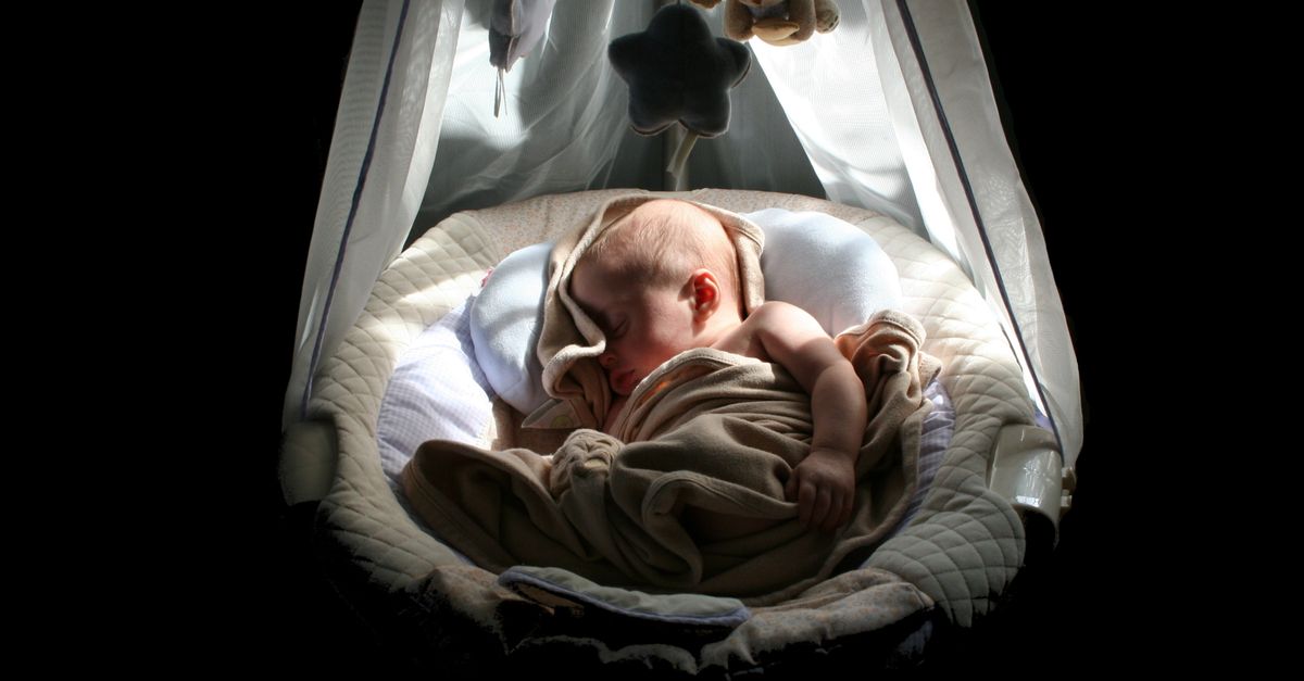 A calm baby sleeps soundly in a cozy, well-lit cradle under a mobile.