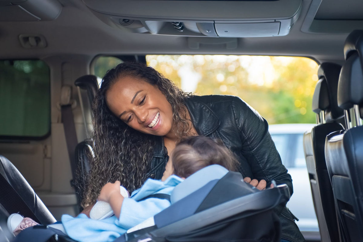 A smiling mother leans in to check her baby in an infant car seat