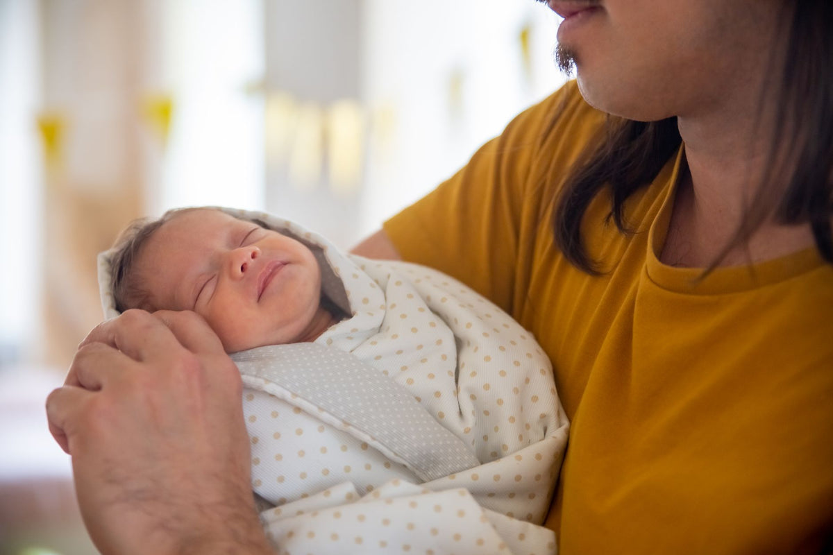 A parent cradles a sleeping newborn swaddled in a soft spotted blanket