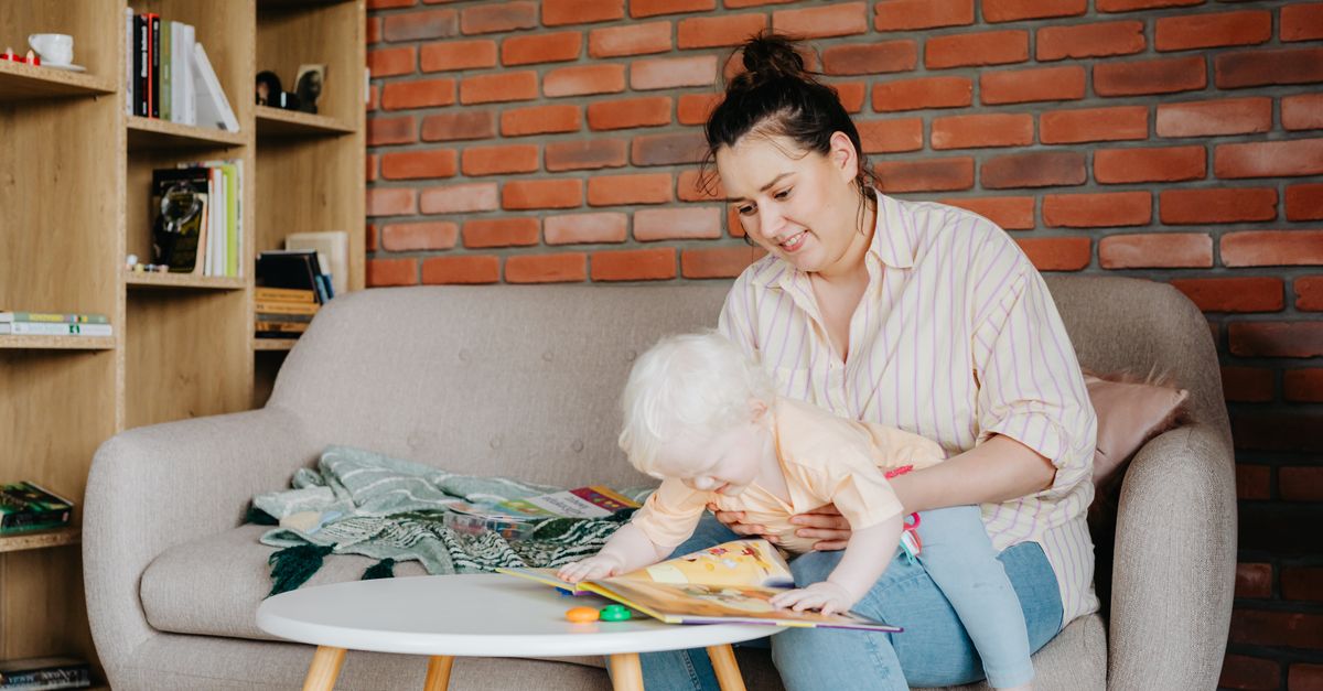 A mother lovingly reads to her baby on a comfortable sofa, surrounded by bookshelves in a cozy living room.