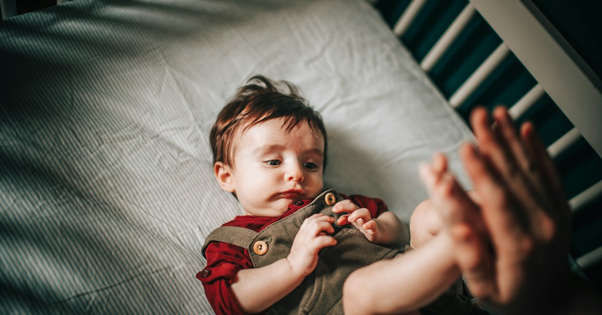 Baby in gray shirt lying on bed