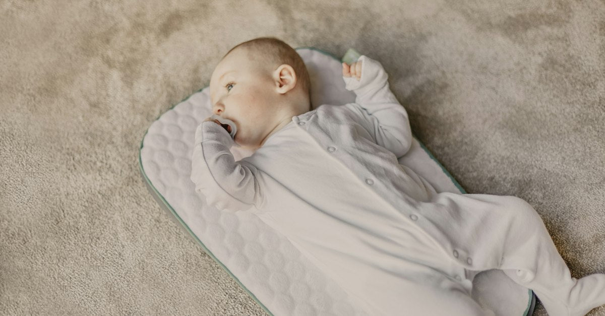 Baby in white onesie lying on white and blue bed