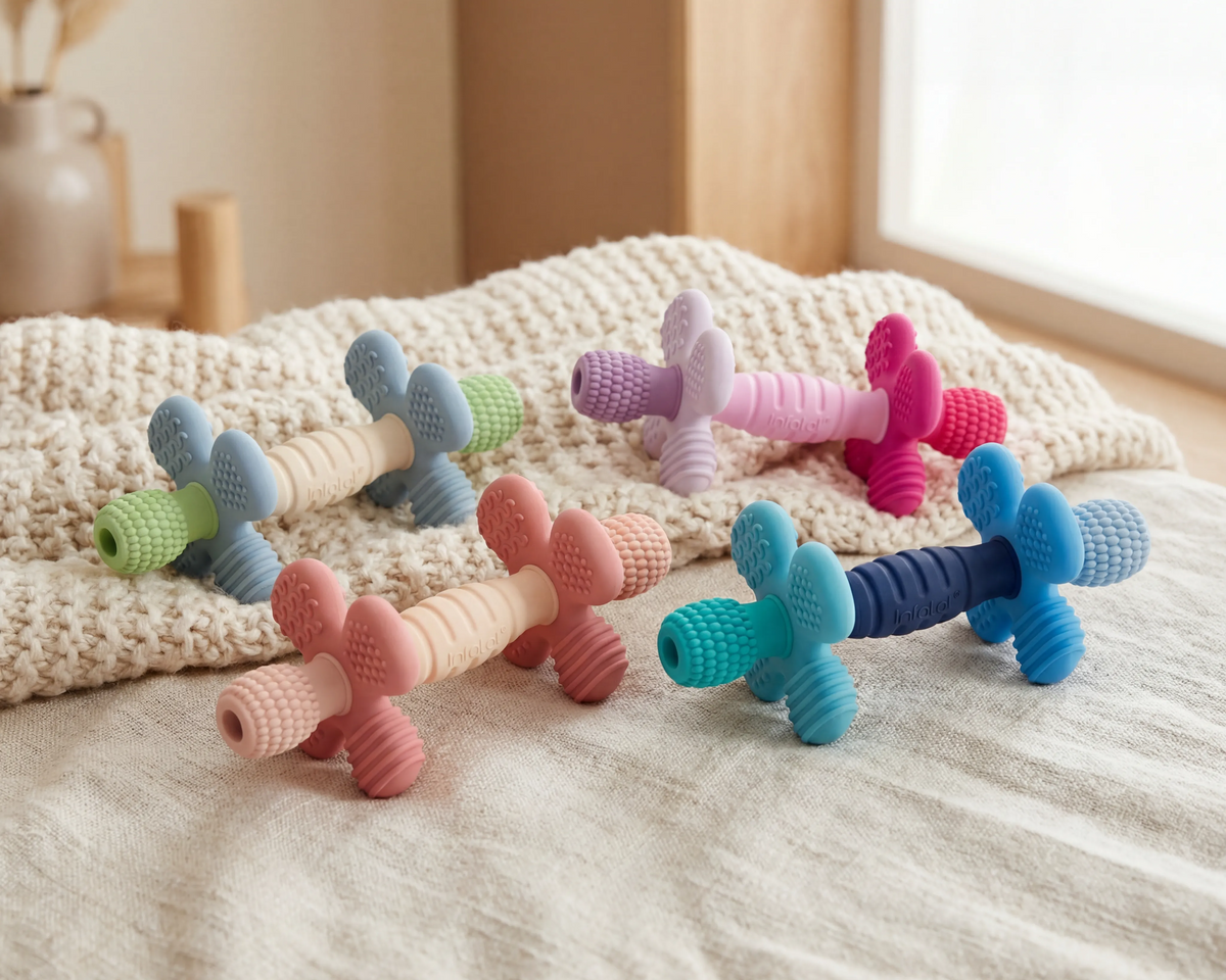 Barbell Buddy teethers in four colour combinations arranged on a knitted blanket