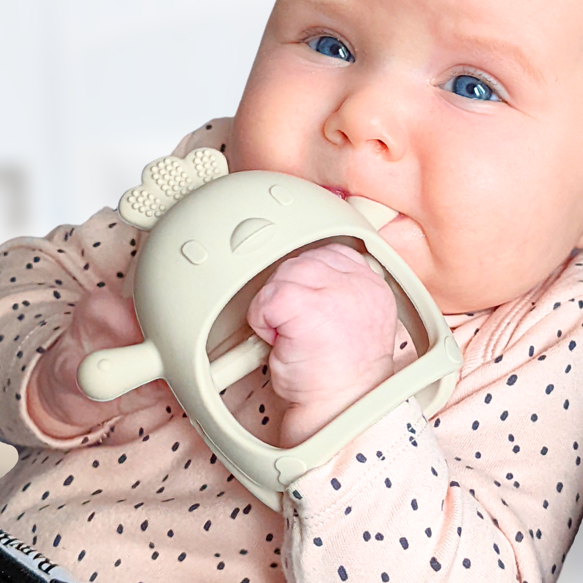 Baby wearing the Infatot Chicken Teething Mitten in Cream, held to the mouth with the hand inside the mitten