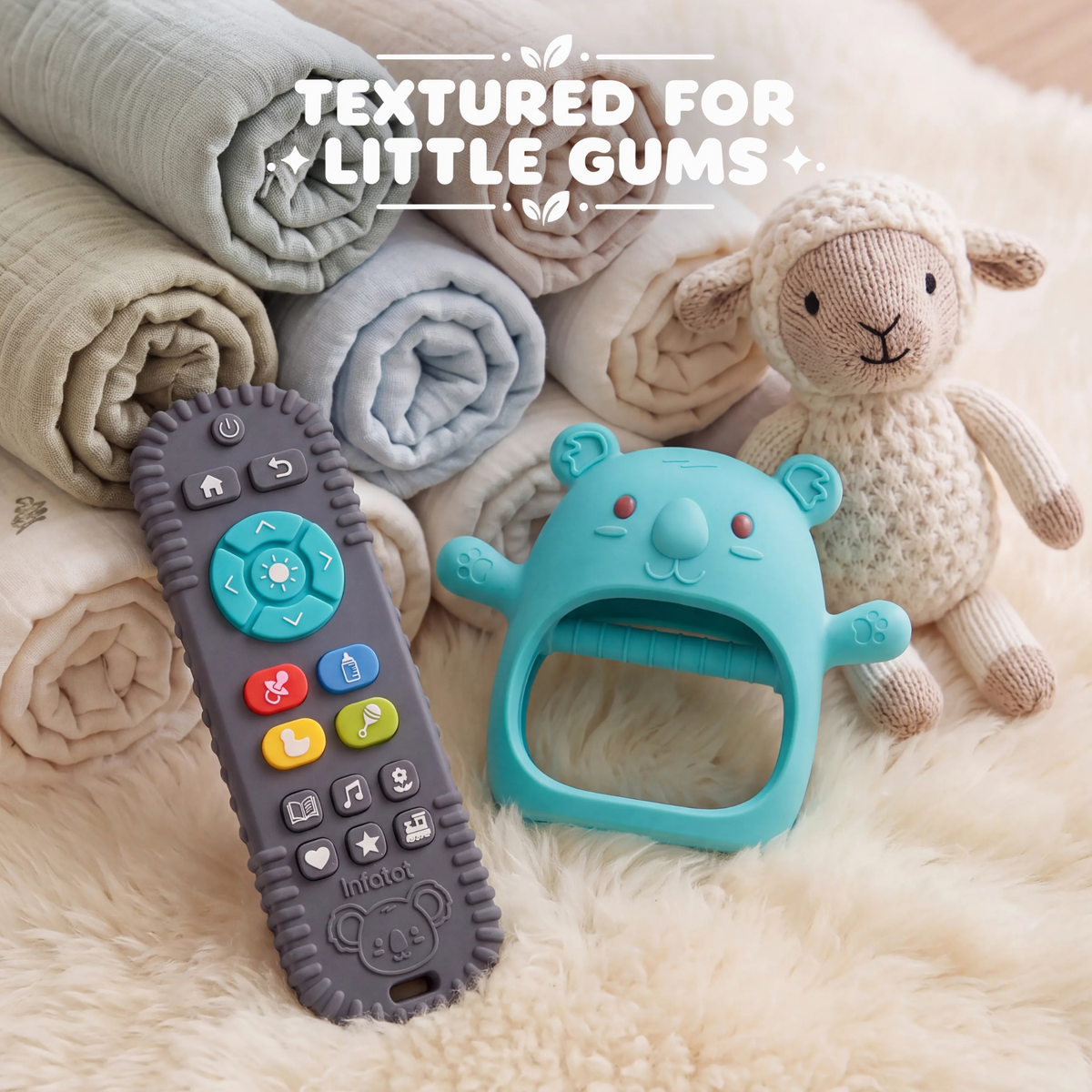 Teal Koda Koala mitten and remote-shaped teether on blankets beside a teddy bear