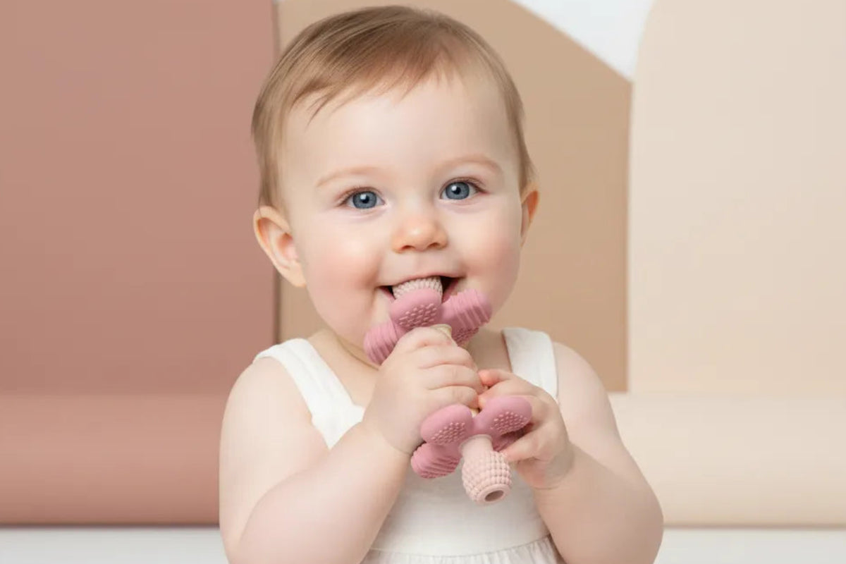 Baby holding and chewing a pink Barbell Buddy teether