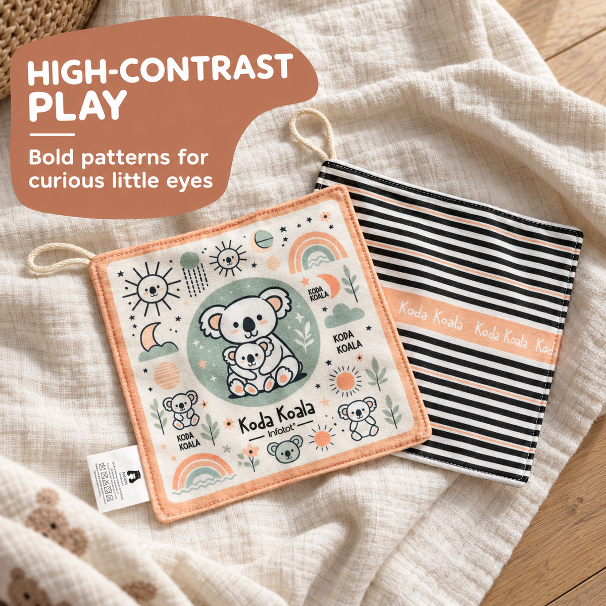 Two soft baby fabric play mats laid on a textured cream cloth over a wood surface. The front mat is cream with peach border and koala/rainbow/sun illustrations, and the back mat is black-and-white striped with peach text reading 'Koda Koala.