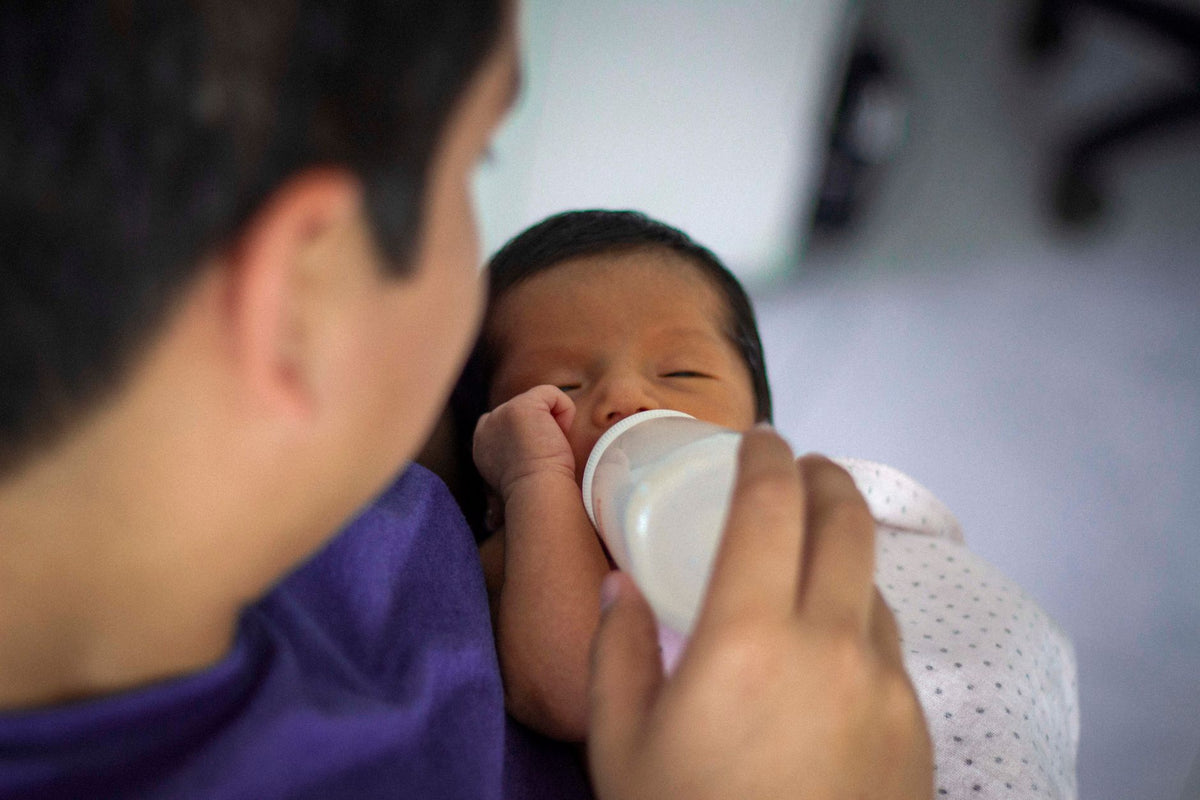A father feeds his newborn baby a bottle while holding them fairly upright