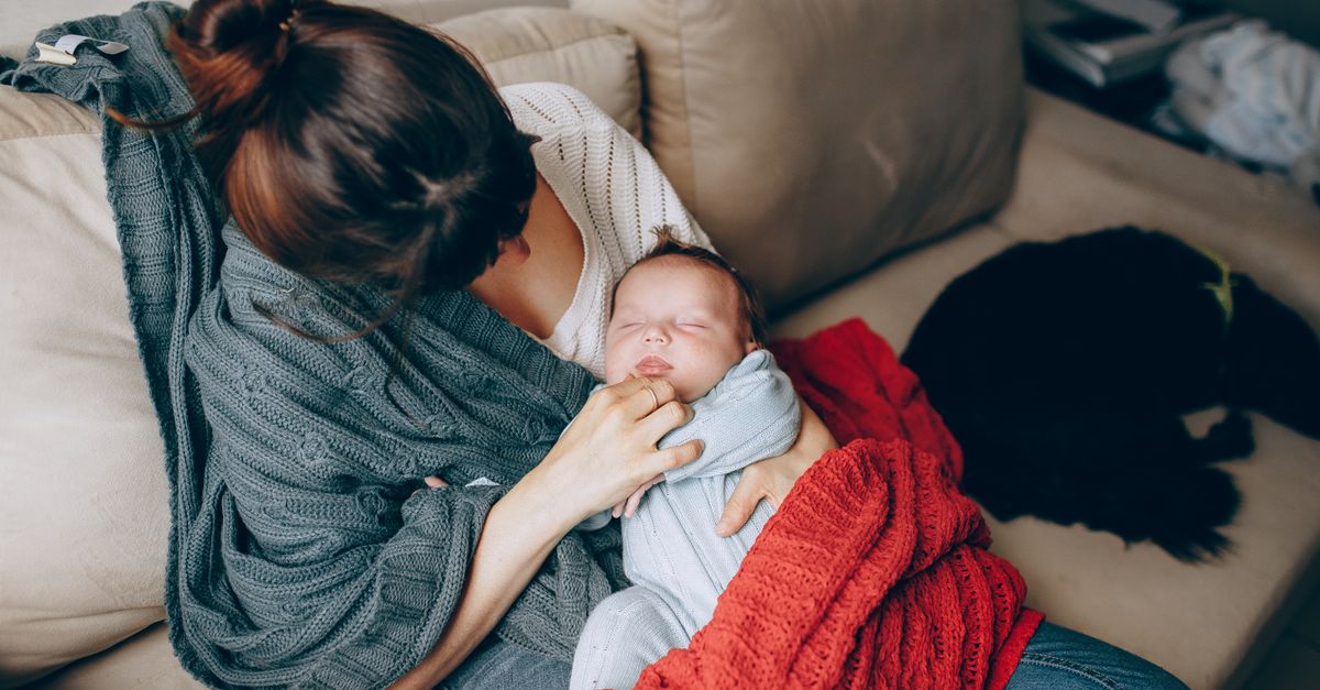 A tender moment of a mother comforting her sleeping baby while resting on a sofa indoors.