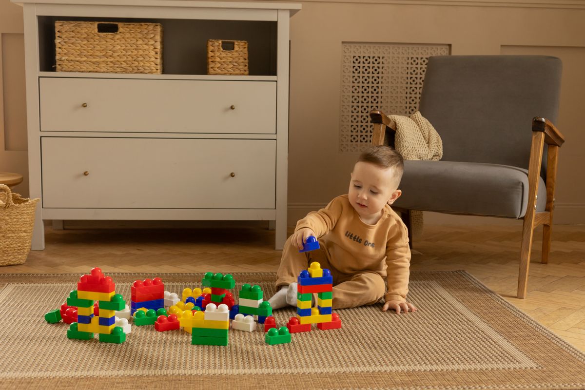 Baby sitting on a nursery rug playing with colourful building bricks