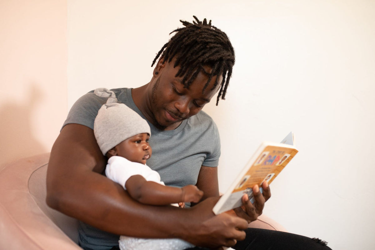 A father reads a picture book to his baby, cuddled safely in his lap
