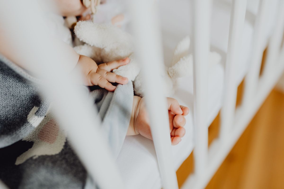 Newborn baby sleeping on their back in a clear cot beside a softly lit bed