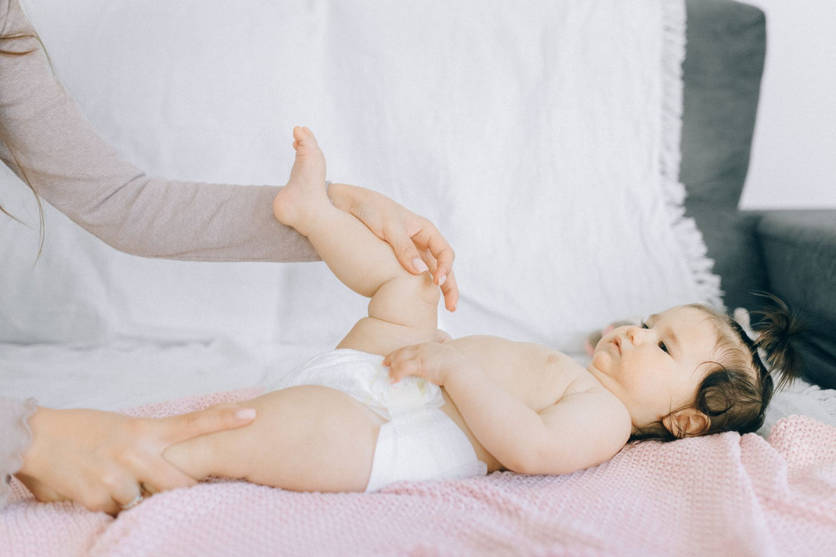 A parent gently massages the legs of a baby lying on a pink blanket
