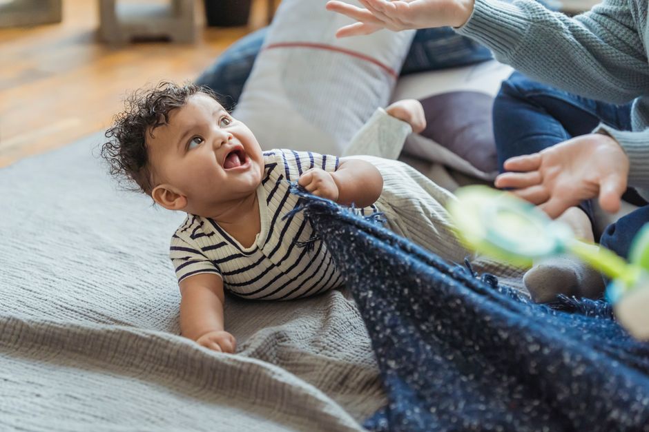 A baby does tummy time on a grey blanket on the floor beside a parent