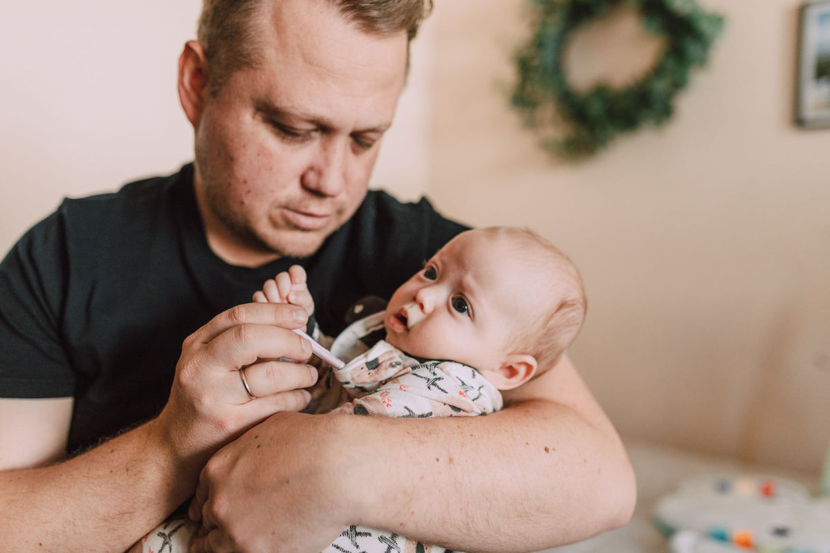 A father holds his baby close while taking the baby's temperature under the arm