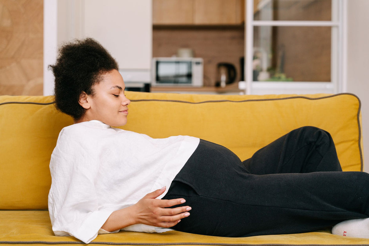 A pregnant woman rests on her side on a sofa with a hand on her bump