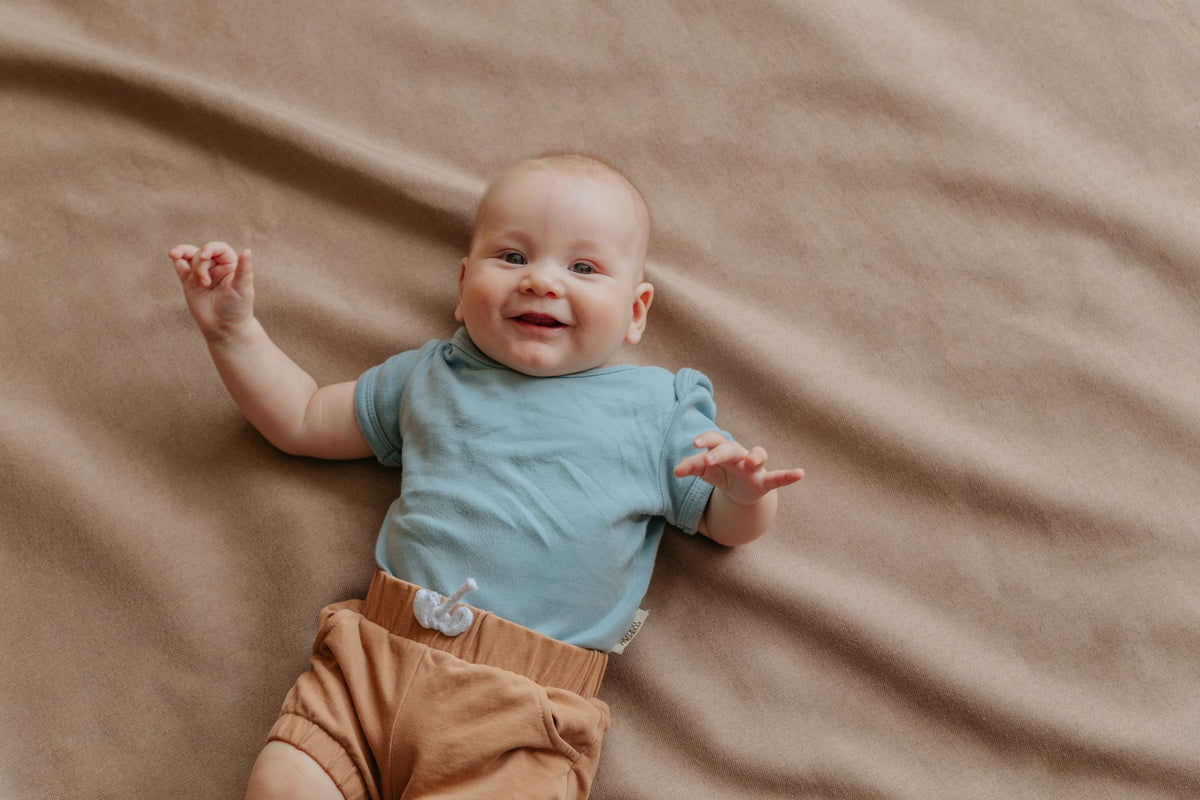 A smiling baby lies on their back on a soft brown blanket