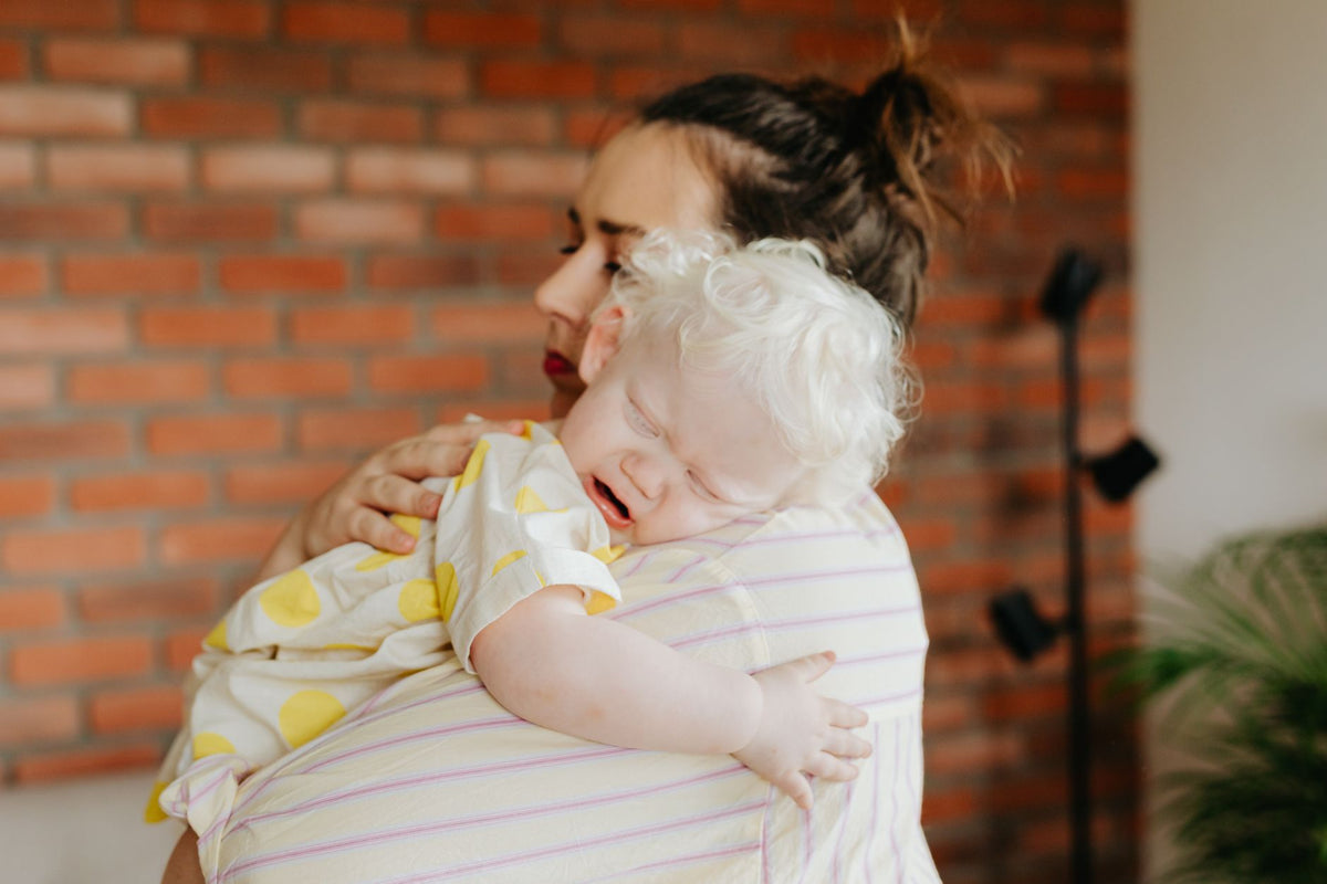 A mother cuddles her crying baby upright against her shoulder to comfort them