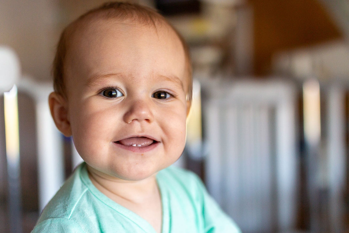A smiling baby shows their first two bottom teeth in a bright room