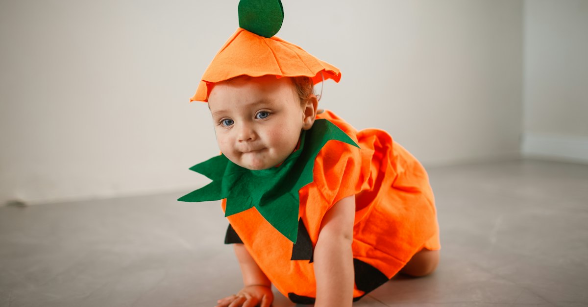A baby dressed in a carrot costume crawling on the floor