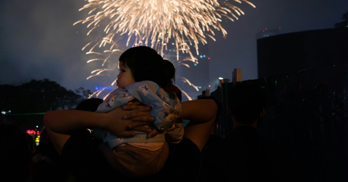 A child on shoulders watching fireworks explode at night