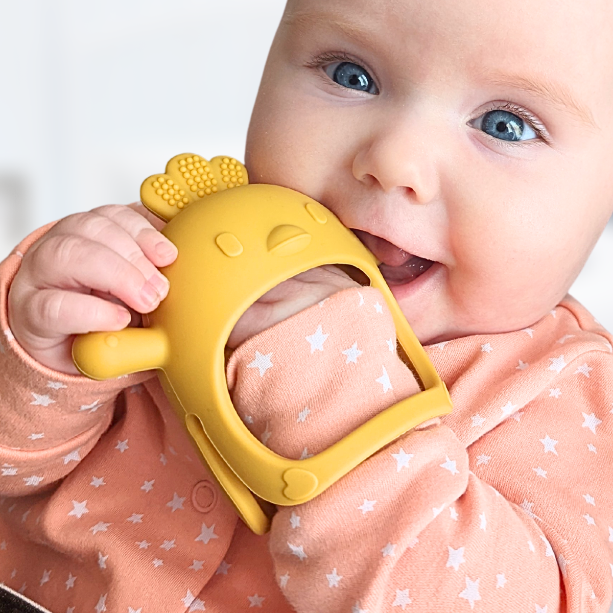Baby wearing the Infatot Chicken Teething Mitten in Yellow, held to the mouth with the hand inside the mitten