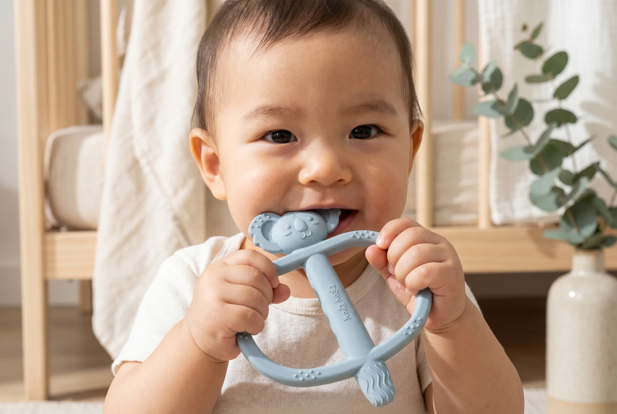 Baby holding and chewing a blue Koda Koala Bitey teether in a nursery