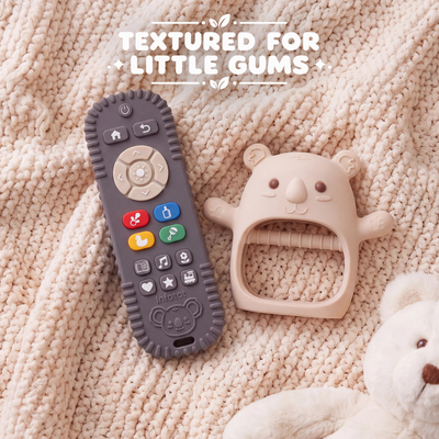 Cream Koda Koala mitten and remote-shaped teether resting on a knitted blanket