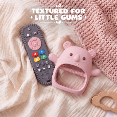 Plum Koda Koala mitten and remote-shaped teether resting on a knitted blanket