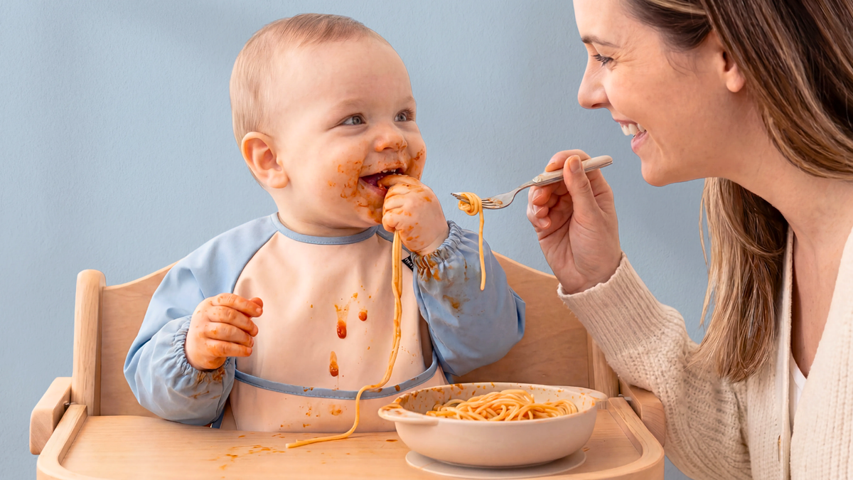Parent feeding a baby wearing an Infatot coverall bib with blue sleeves