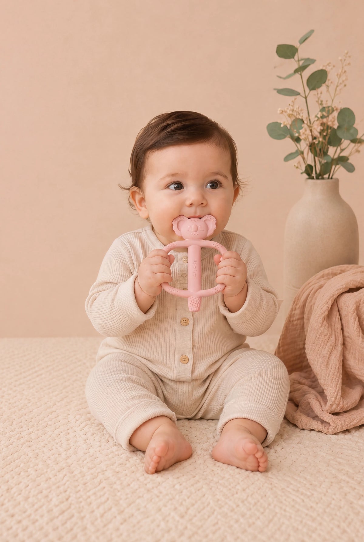 Baby sitting on a rug and holding a pink Infatot teether
