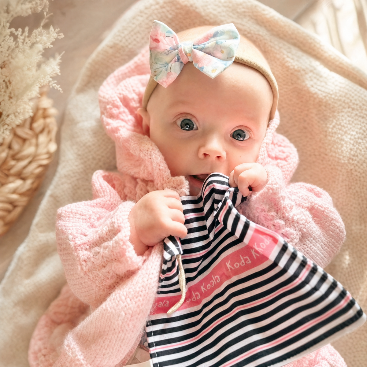 Baby holding a black-and-white striped Infatot crinkle sheet with pink edging