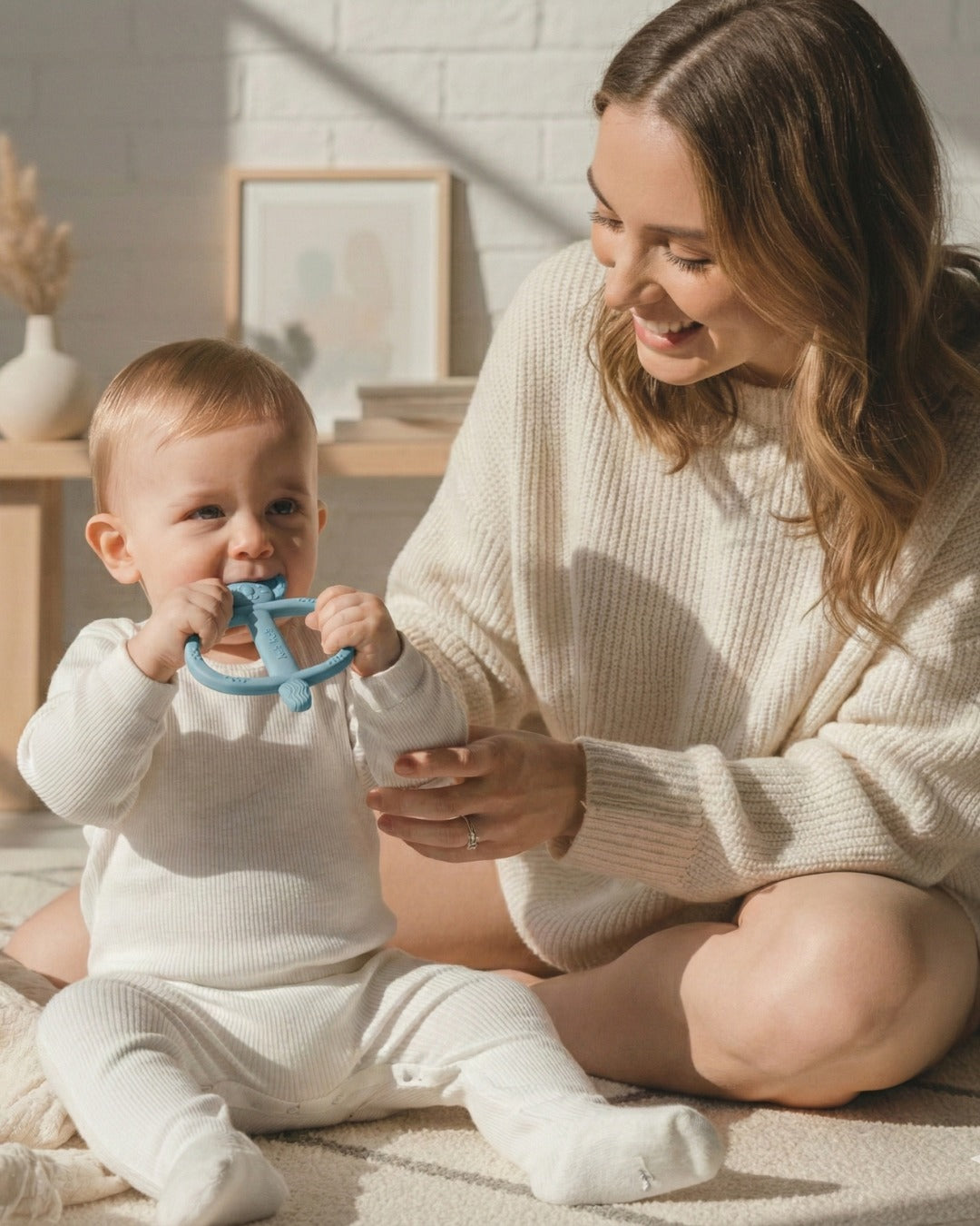 Parent sitting beside a baby holding a blue Koda Koala Bitey teether