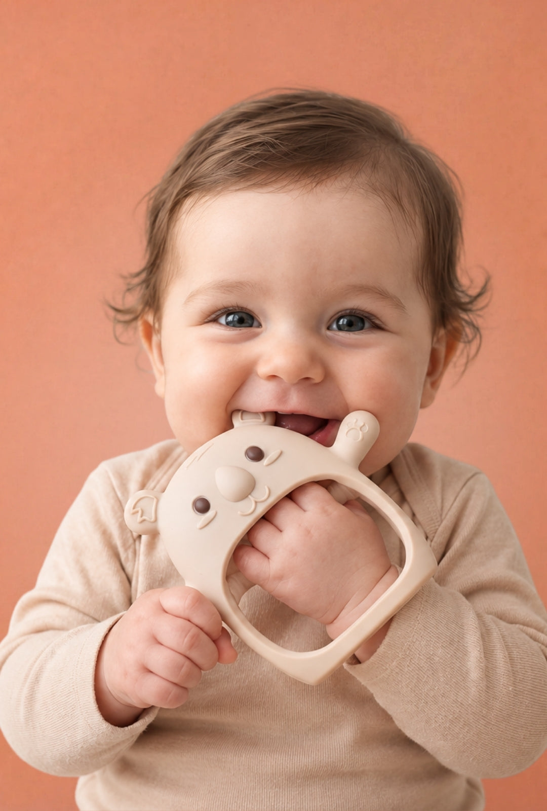 Baby holding a cream Koda Koala teething mitten against an orange background