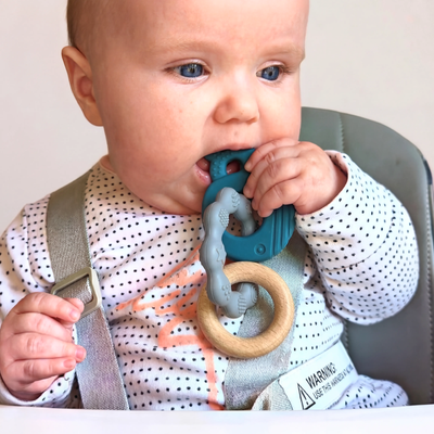 Baby in a highchair chewing the blue whale-shaped part of the MultiTexture Sea Teether